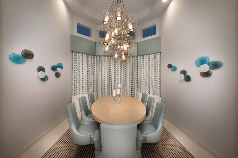 Pale aqua curved dining chairs around an oval wooden table beneath a cluster of clear globe pendants.