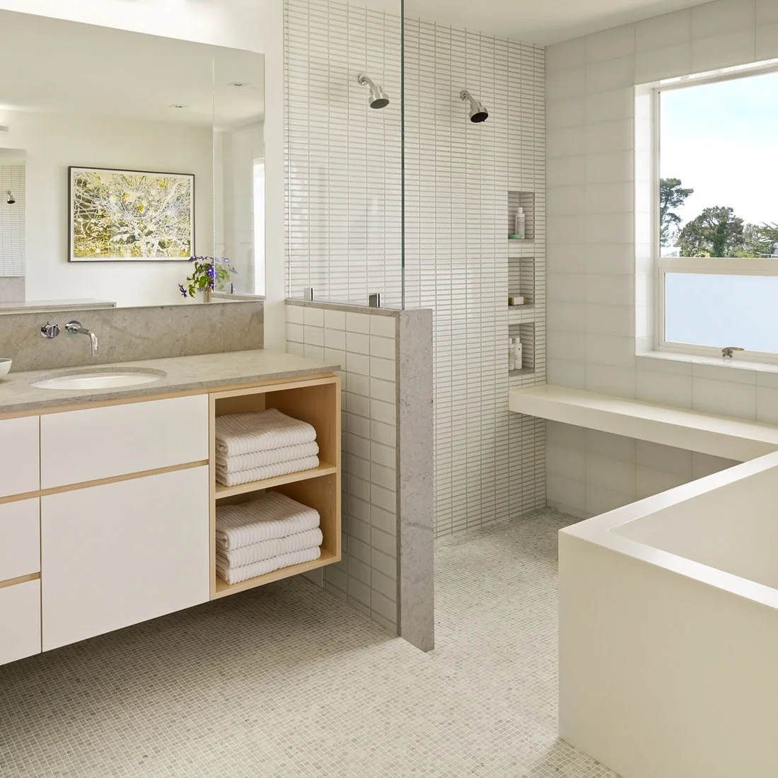 Fine pale mosaic floor tiles meet narrow shower wall tiles beside a white vanity with open timber shelves.