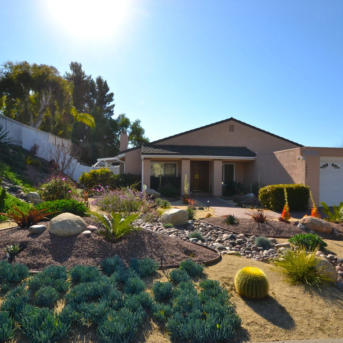 A front garden with curved gravel beds, a broad channel of rounded stones, boulders and spaced sculptural plants.