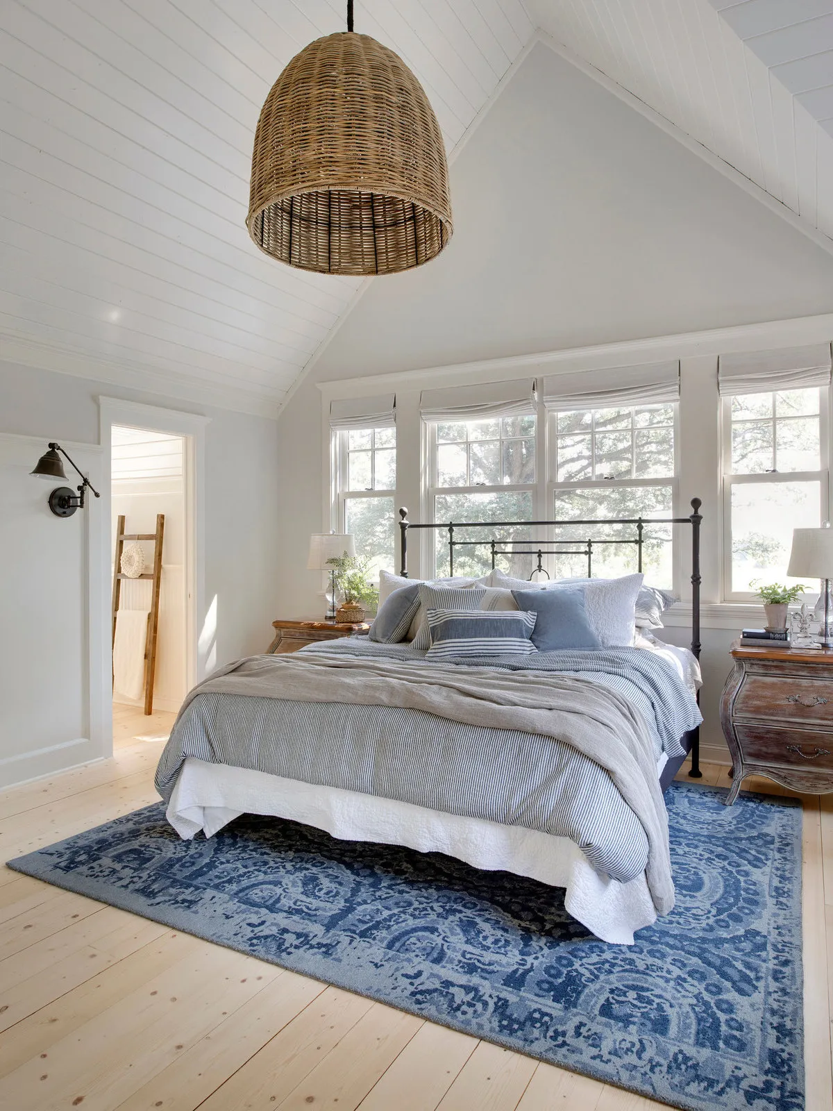 A woven pendant hangs over pale bedding and a blue patterned rug.