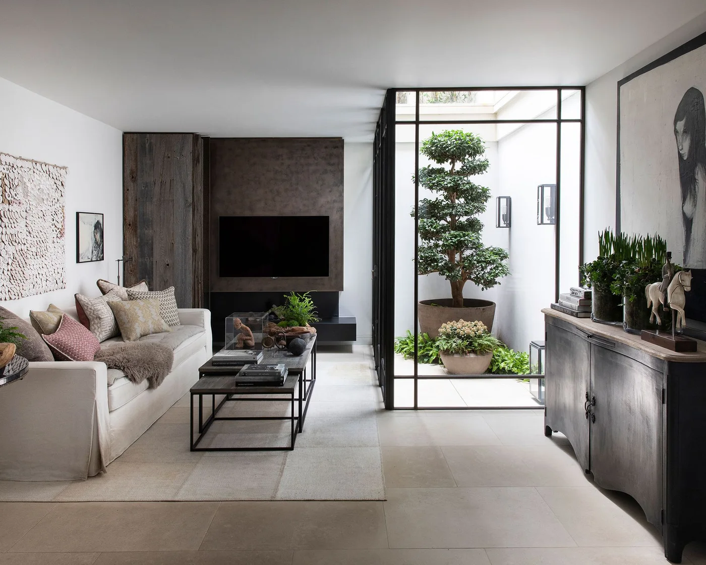 Dark TV panel and low cabinet beside a glazed courtyard wall and pale sofa
