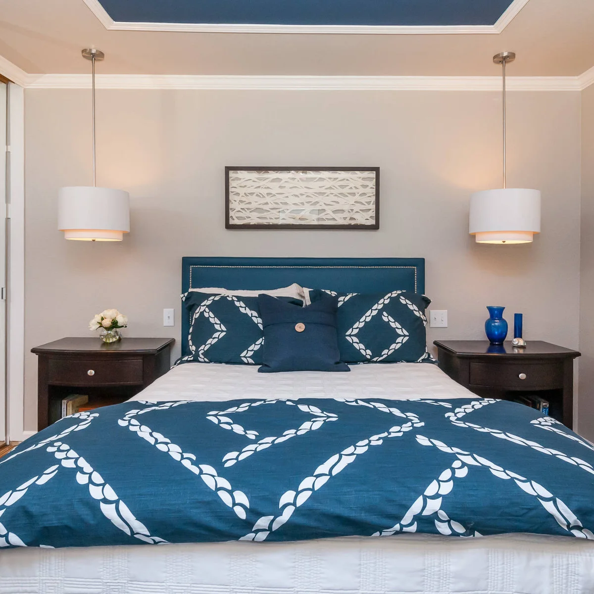 Blue ceiling inset above a bedroom with a blue patterned bedspread and dark wooden bedside tables.
