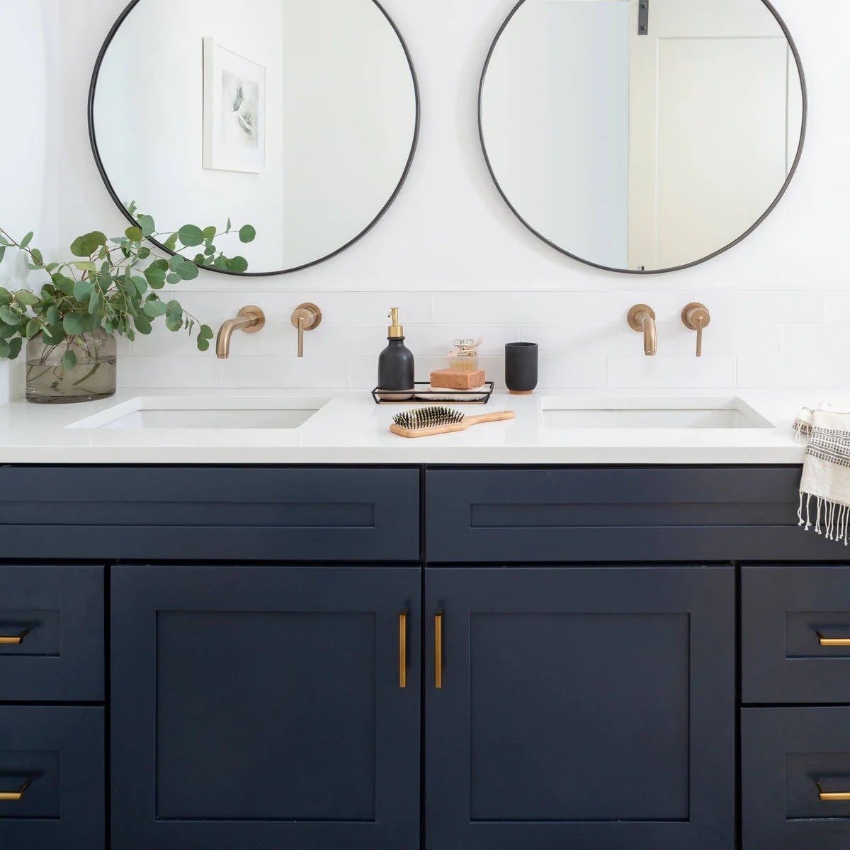 Two black-rimmed round mirrors above a dark blue double bathroom vanity