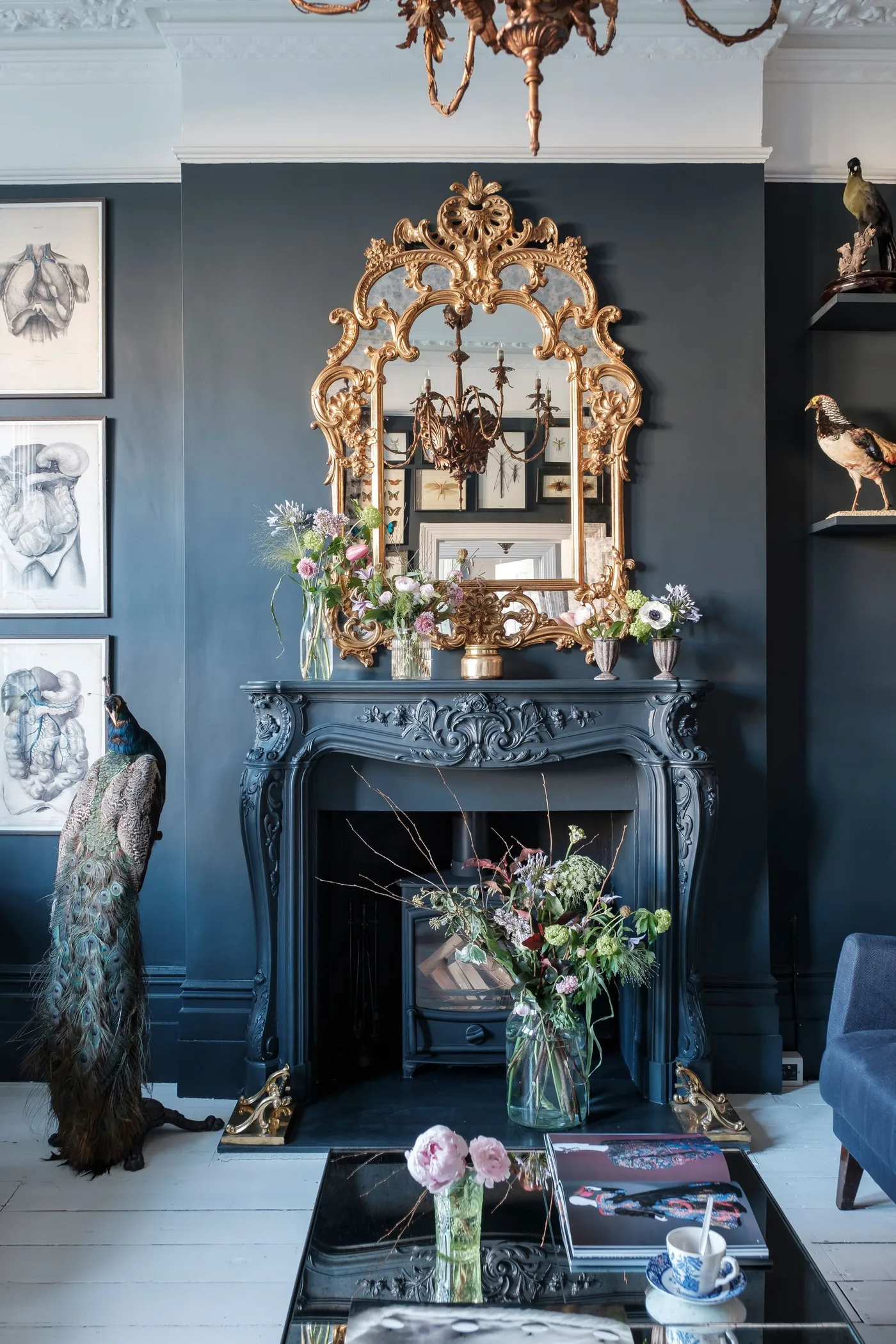 Deep blue fireplace wall and matching ornate mantel with tall gold-framed mirror and flowers