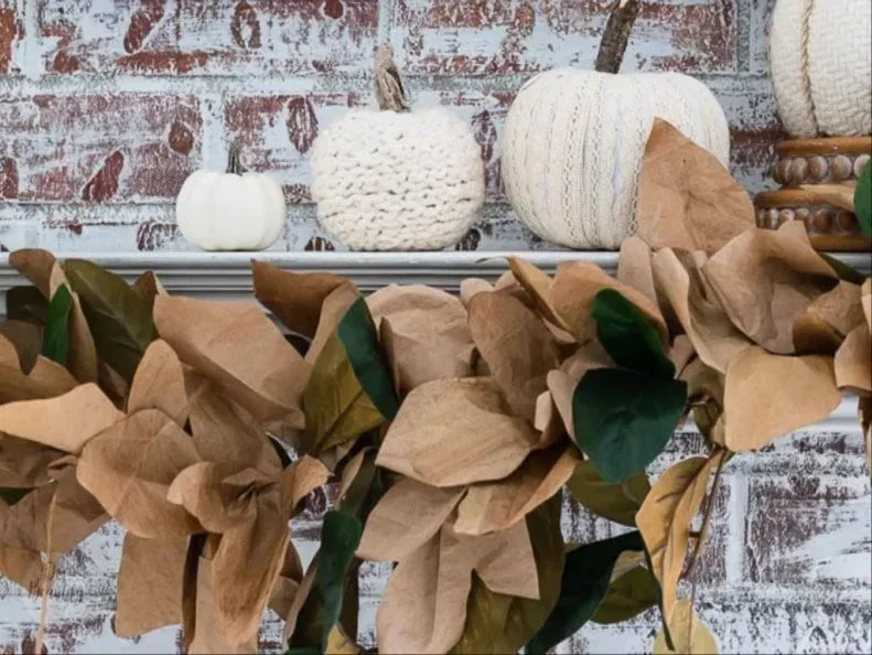 Brown paper leaf shapes and a few dark green leaves gather along a pale mantel above a dark fireplace opening