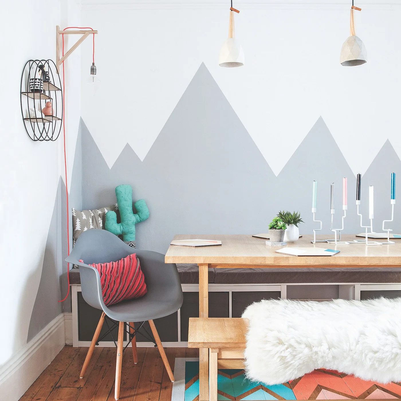 Gray mountain shapes decorate the wall behind a bench and wood dining table with a gray chair, a backless bench and pale hanging lights.