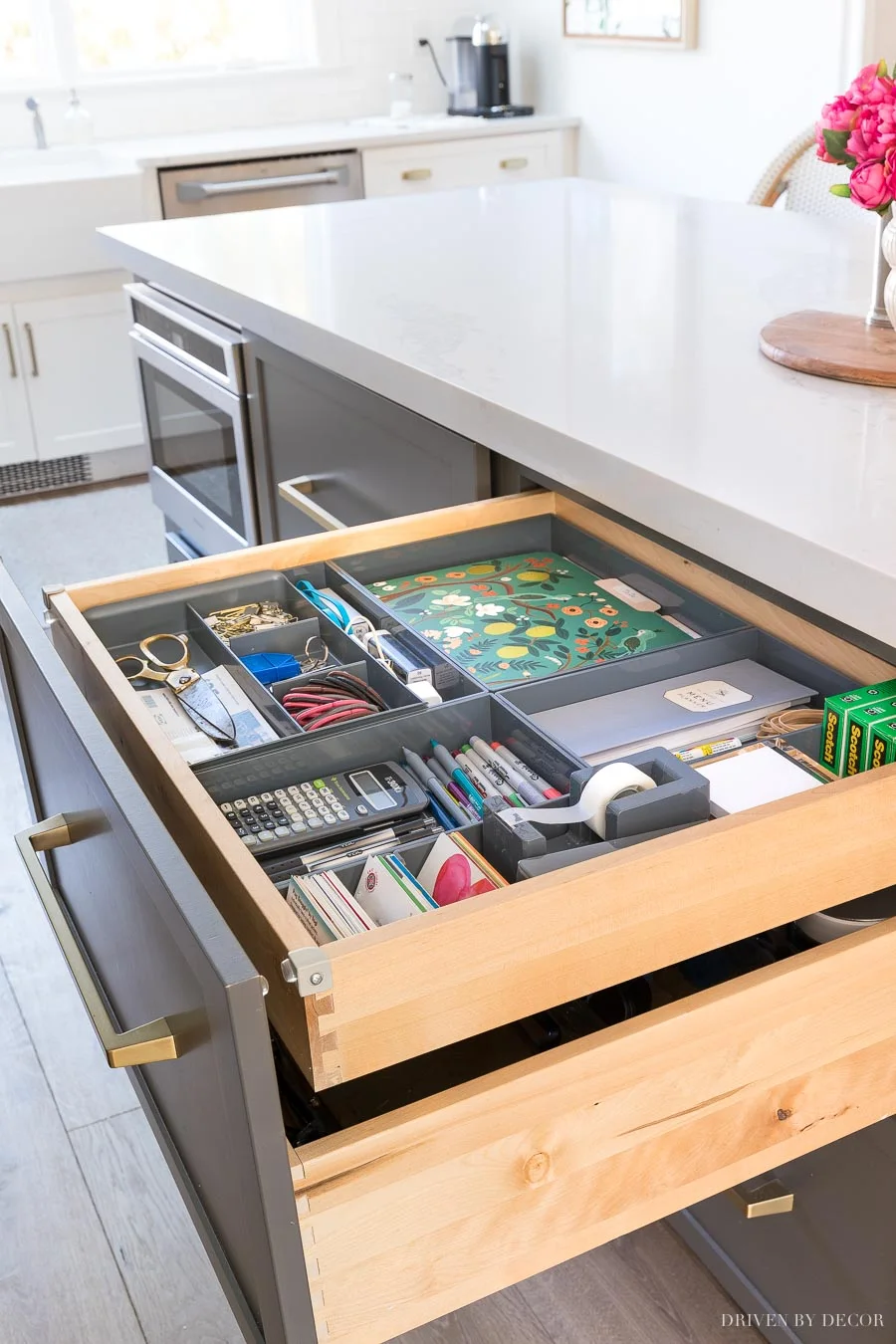 Wide kitchen drawer with gray organizers, scissors, pens, envelopes and a floral folder