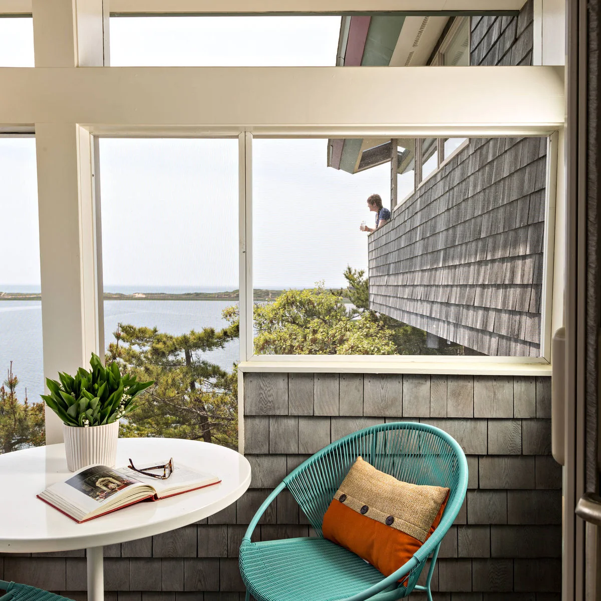 A turquoise woven chair sits beside a white round table on a screened waterside balcony
