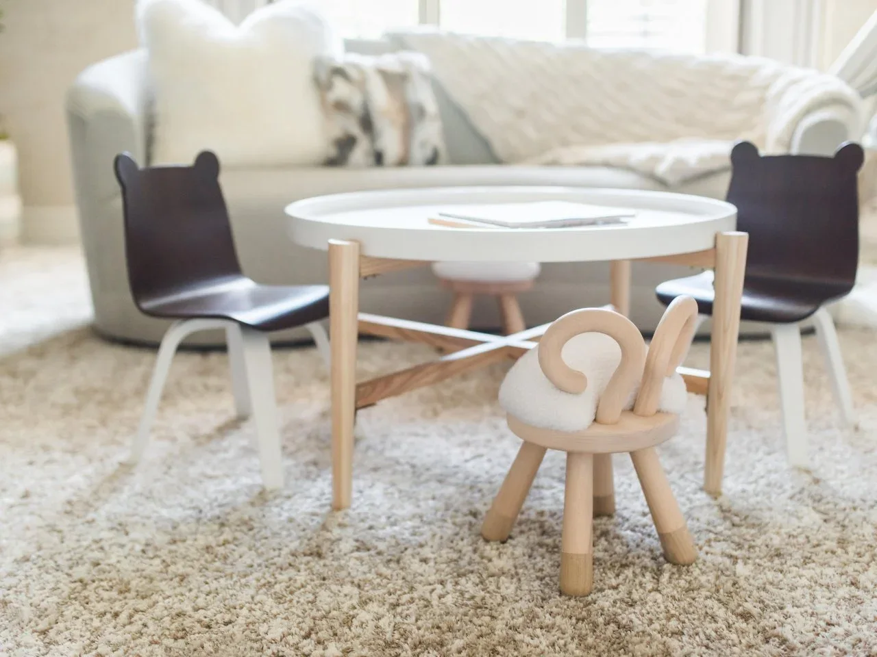 A round child-sized table stands with dark bear-shaped chair backs and a sheep-shaped stool on a pale rug.