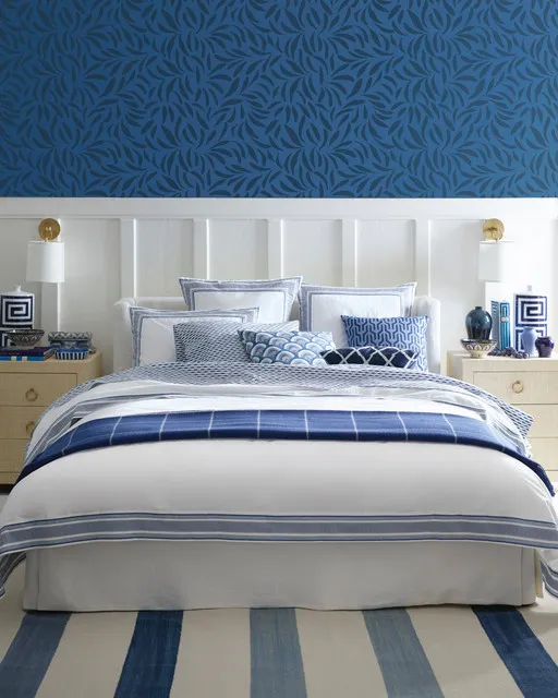 Deep blue patterned wallpaper rises above pale paneling behind striped bedding.