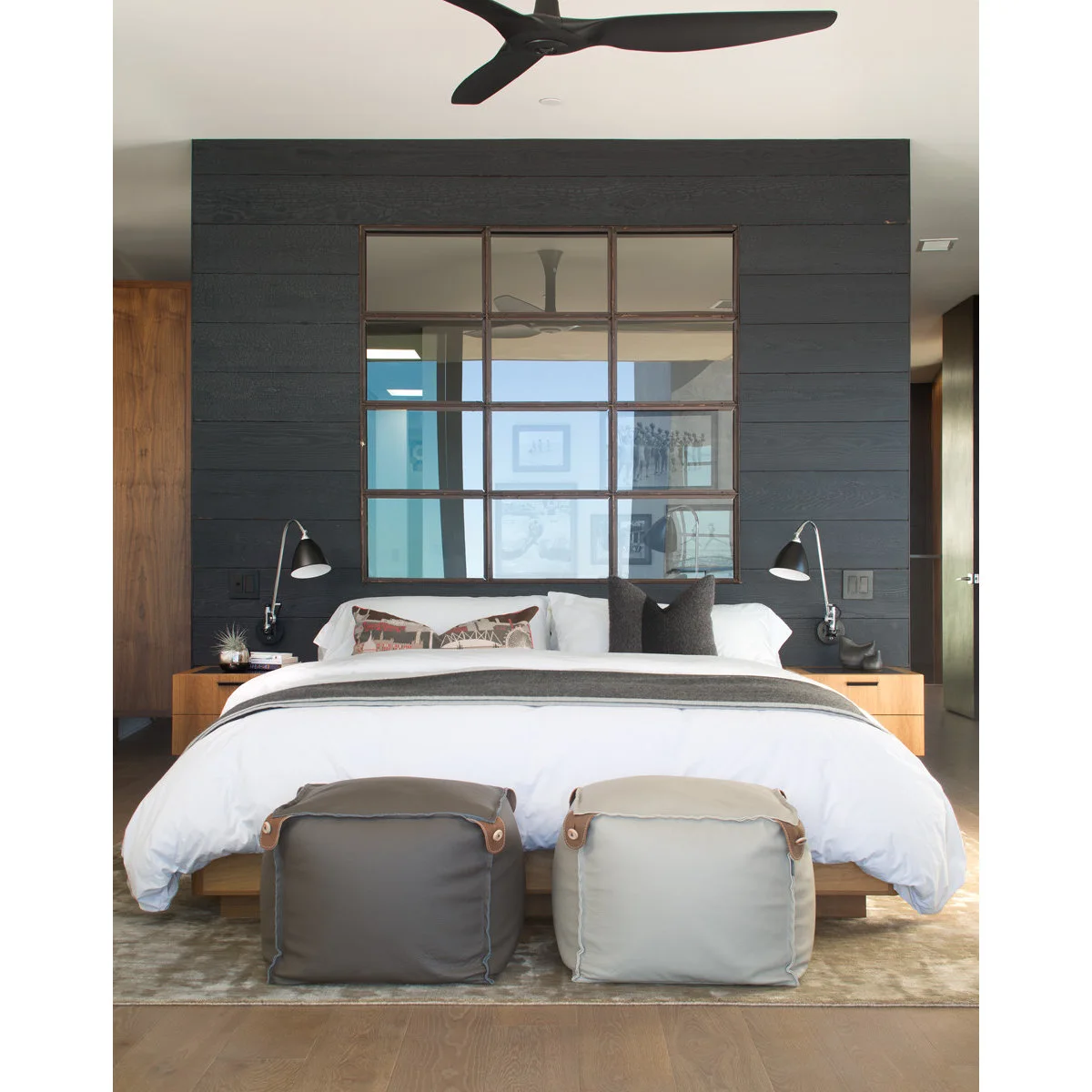 Charcoal horizontal board wall behind white bedding, wood bedside cabinets and a large gridded mirror