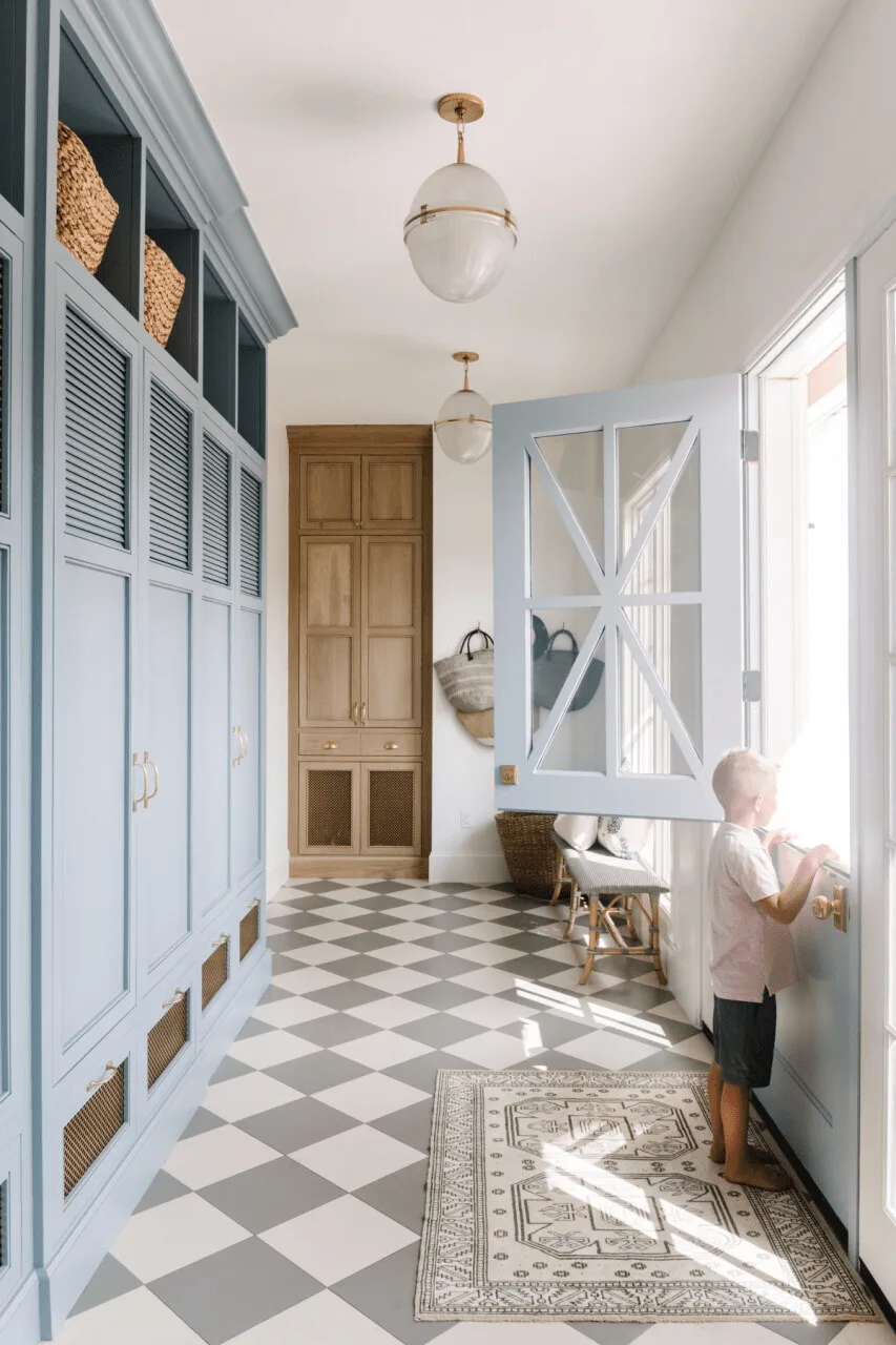 Blue mudroom cupboards with basket cubbies, blue Dutch door and gray-and-white checked floor