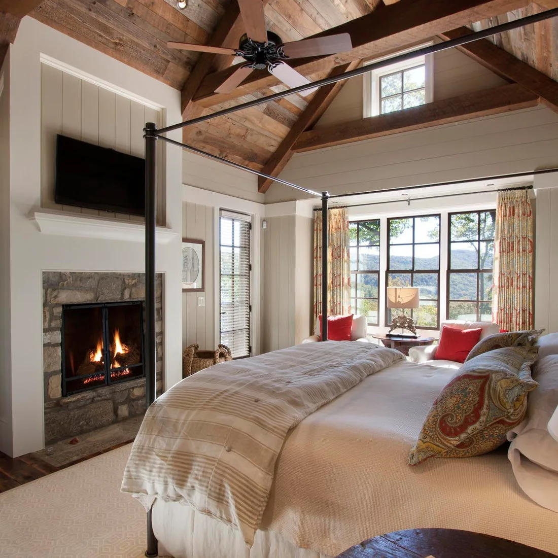 A pale four poster bed with patterned cushions near red window cushions and a timber roof