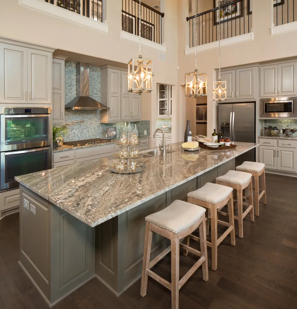 A taupe island with pale stools stands in a double-height kitchen with light perimeter cabinetry