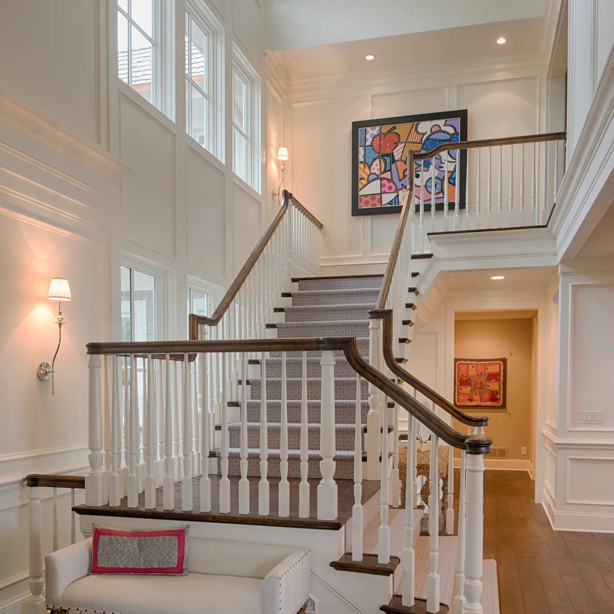 A colorful framed painting hangs on a landing above a diamond-patterned stair runner.
