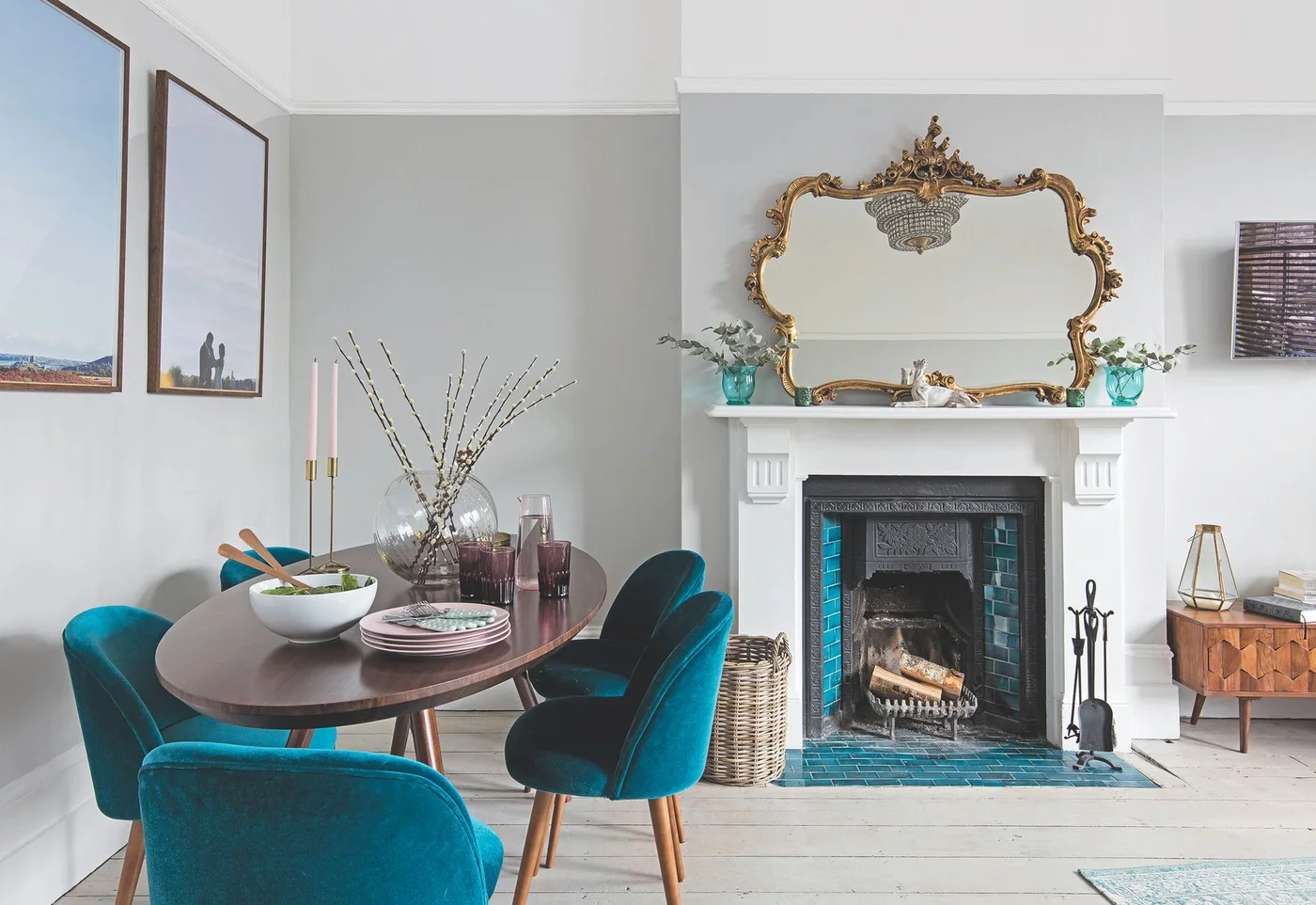 Teal tiles line a fireplace and hearth beneath a white mantel, with teal dining chairs, pale gray walls and an ornate mirror.