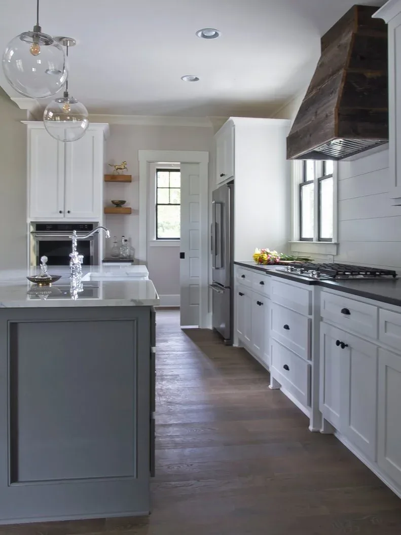 A dark timber hood contrasts with white cabinets, horizontal wall boards and a black kitchen counter.