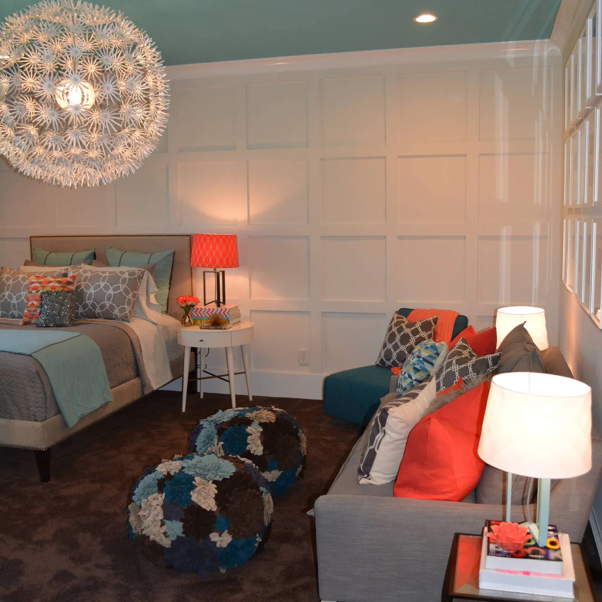 Teen bedroom with a small gray sofa, blue chair and patterned poufs opposite the bed
