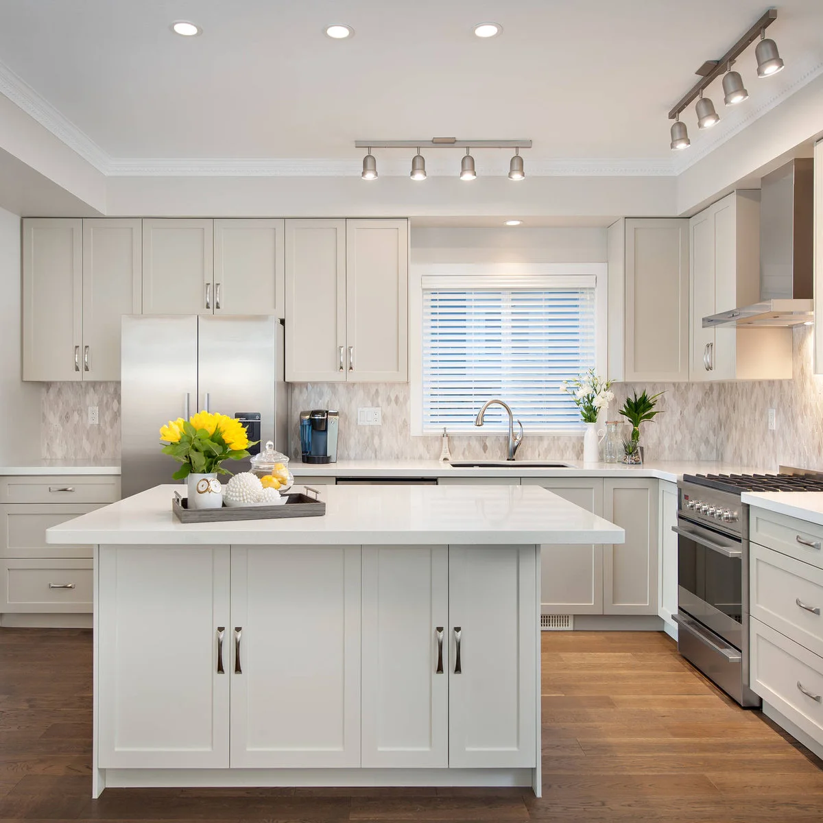 Two short metal ceiling bars with four small shaded heads sit above a pale kitchen alongside round recessed ceiling lights.