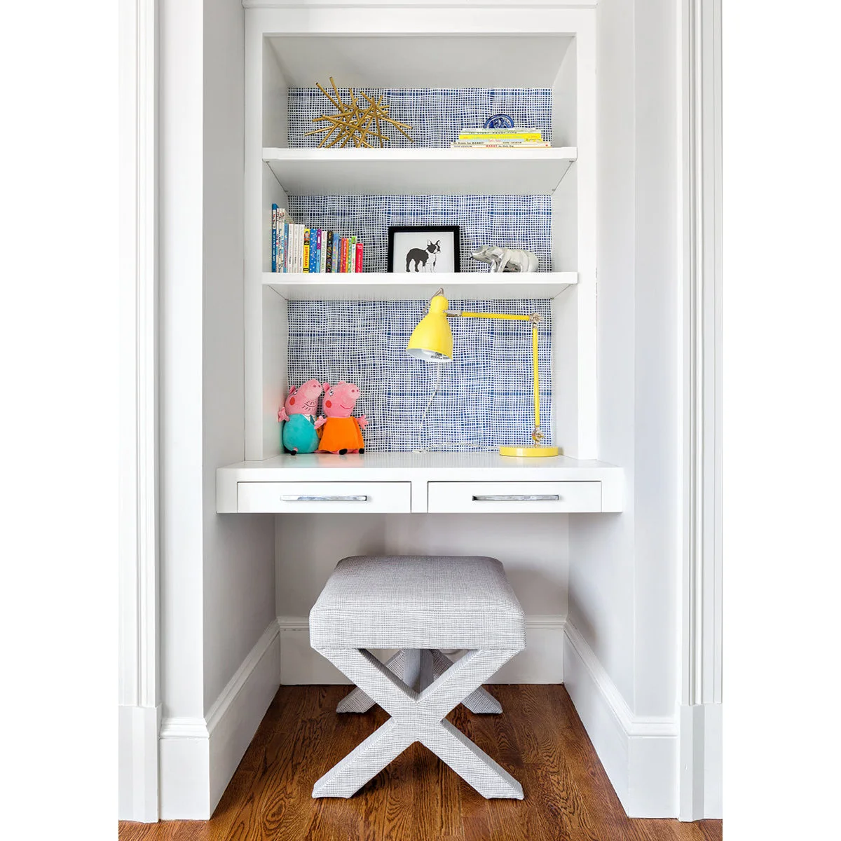 Narrow white floating desk with two shallow drawers, patterned blue backing and a yellow task lamp
