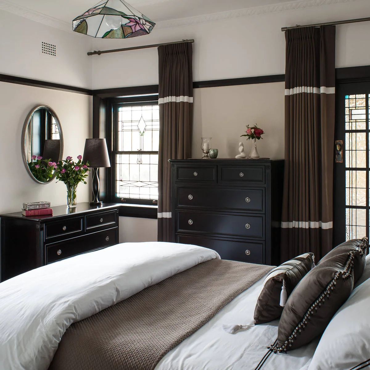Dark brown curtains with light bands beside dark furniture and a bed with a brown runner.