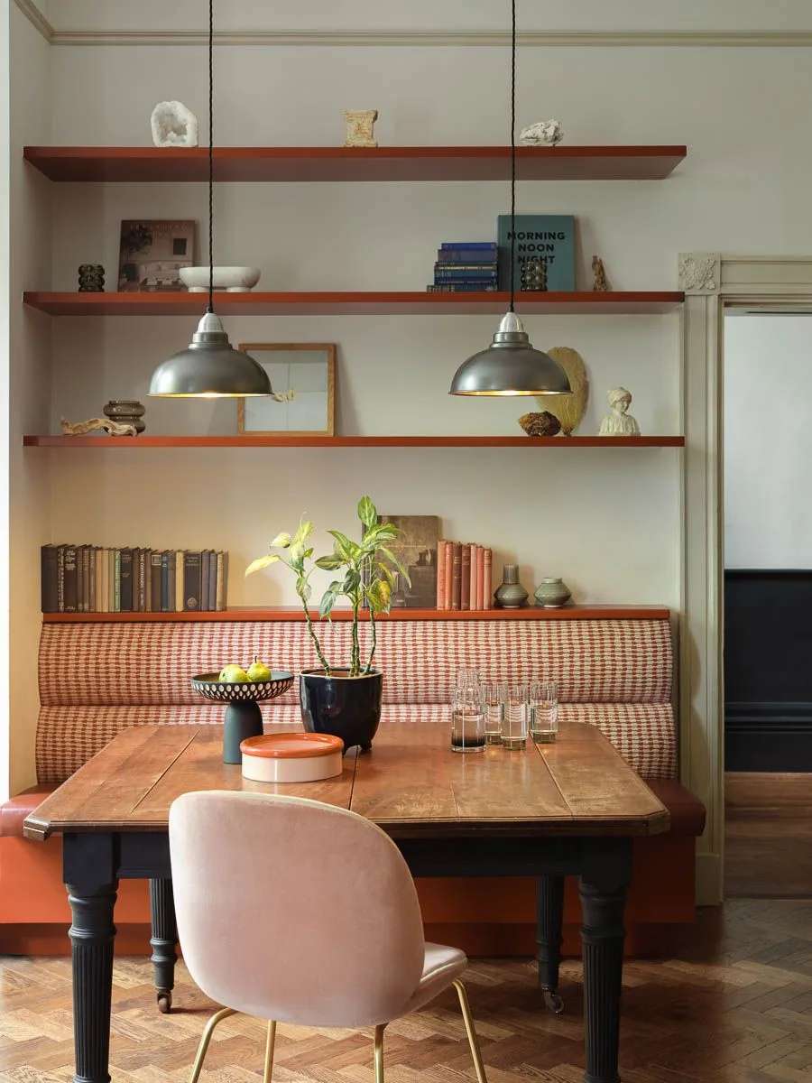 Two metal pendants above a wood table with checked bench upholstery and open wall shelves