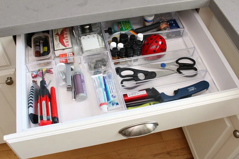 White kitchen utility drawer with clear trays separating scissors, a long lighter, pens and household accessories