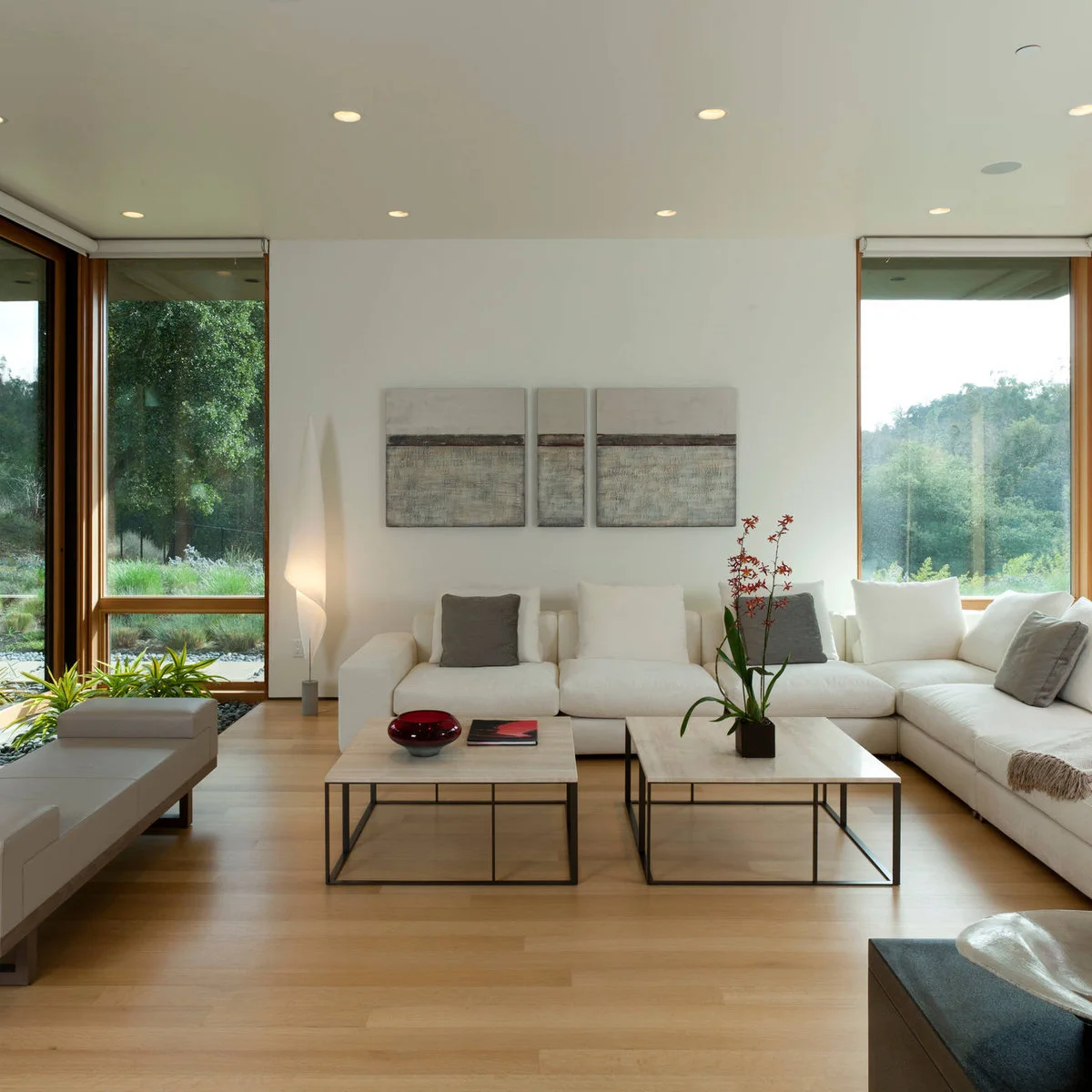 Two square pale coffee tables with a red bowl, a book and a tall flowering plant