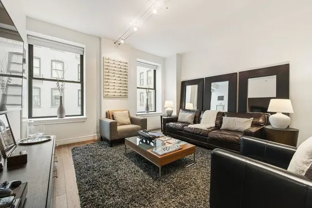 A dark leather sofa sits below two dark-framed mirrors beside pale chairs, table lamps and a wooden coffee table