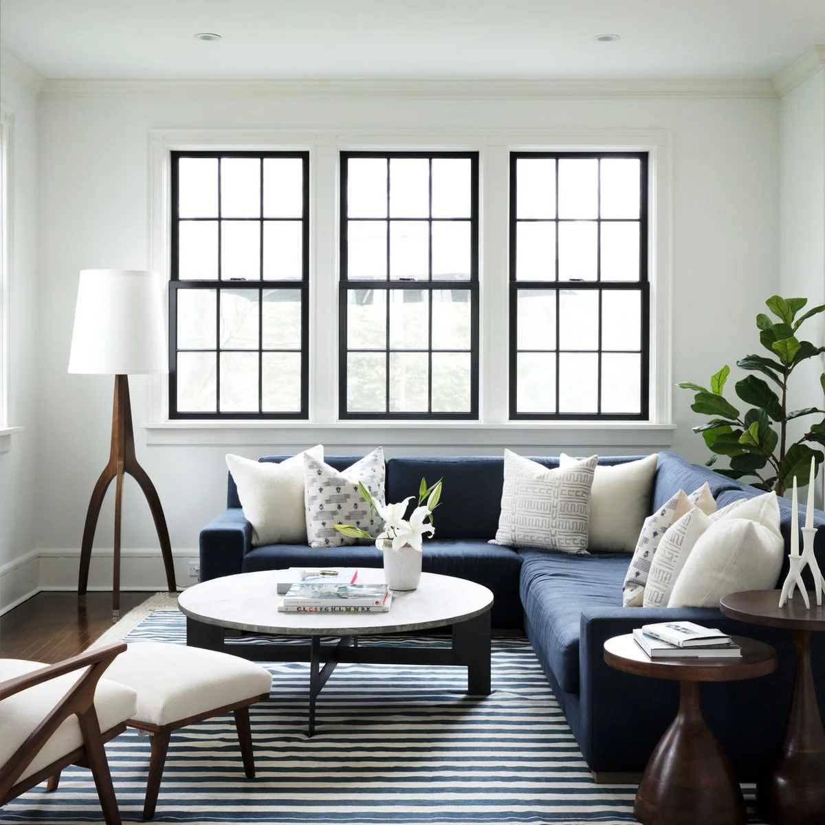 Small white-walled living room with a navy sectional, round pale table and striped rug