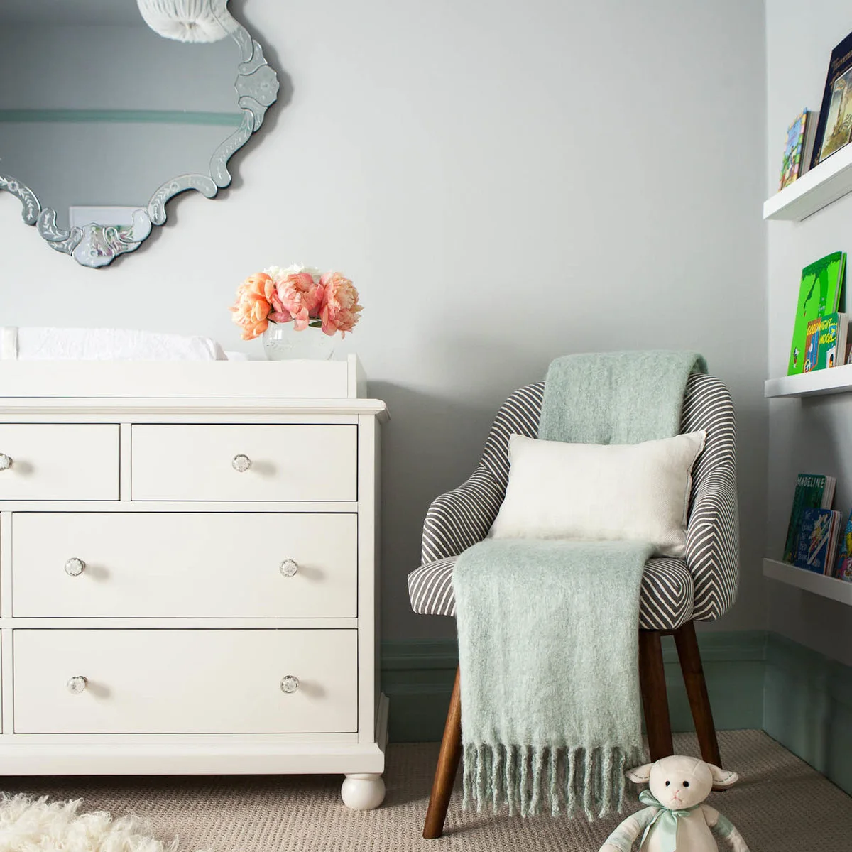 Striped nursery chair with a pale green throw between a white changing chest and wall book ledges