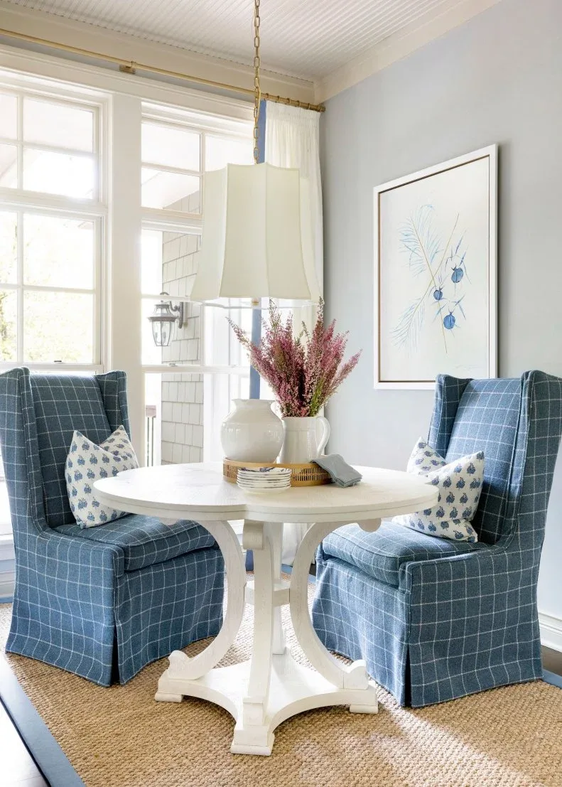 Pale vessels and pink stems grouped on a tray on a white round table between blue checked chairs