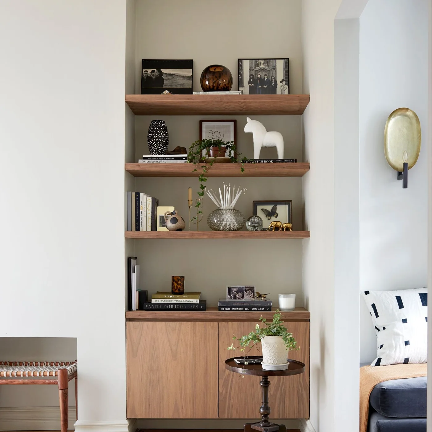 Three timber shelves hold books, framed photographs and small objects above a matching two-door alcove cabinet.