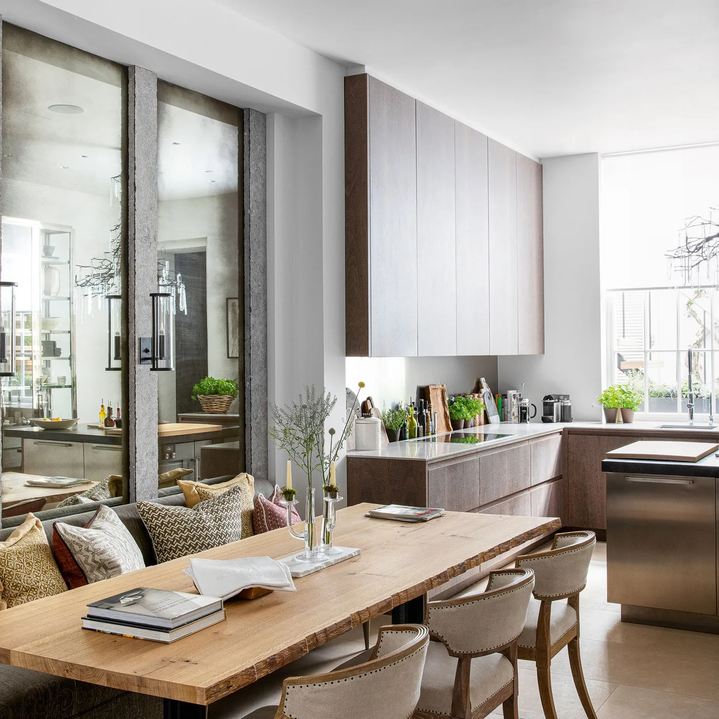 Tall inset mirror panels behind bench seating beside a long wood table in an open kitchen dining area
