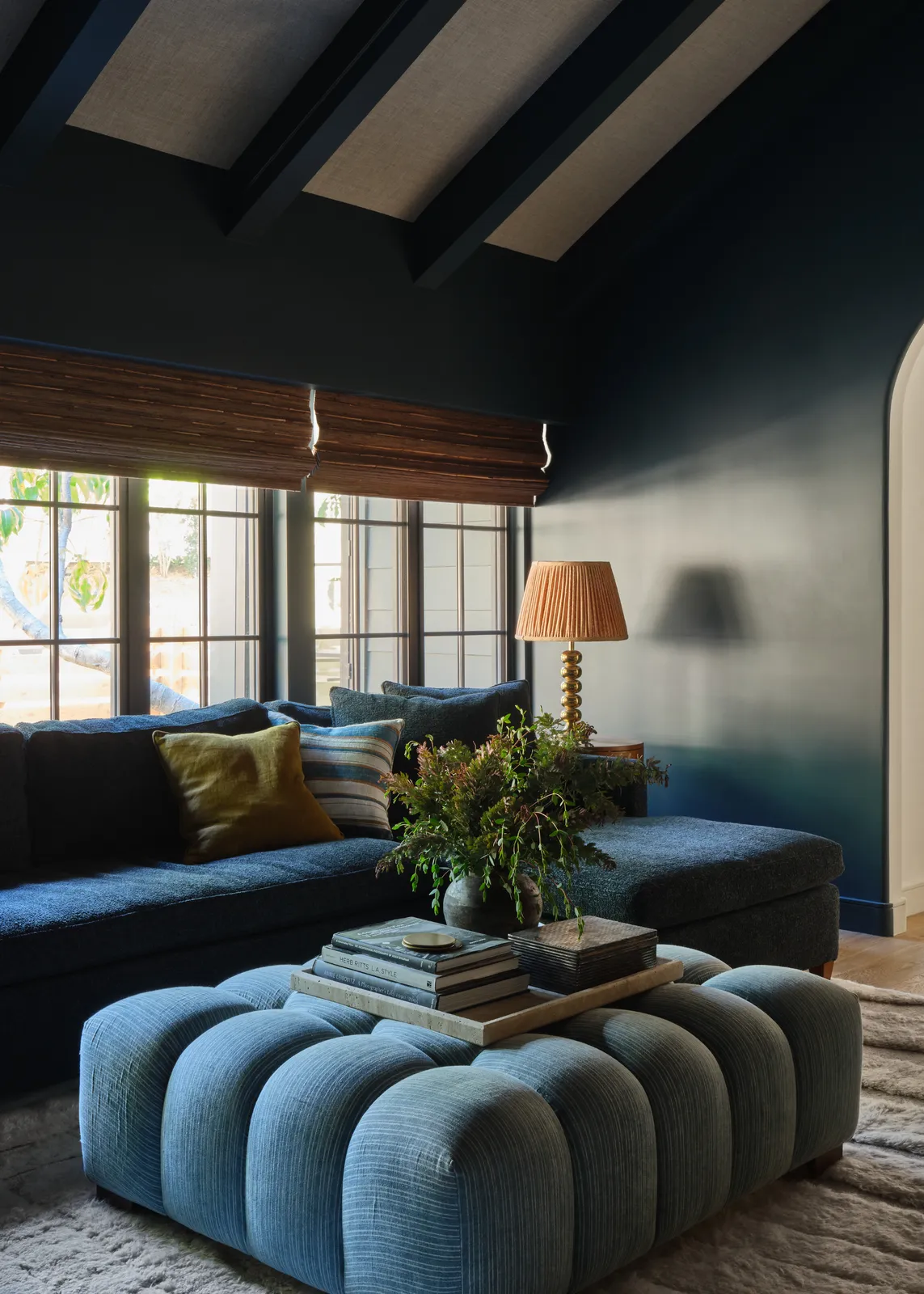 A dark blue sofa sits beside a pale blue rounded ottoman beneath darker walls and beams.