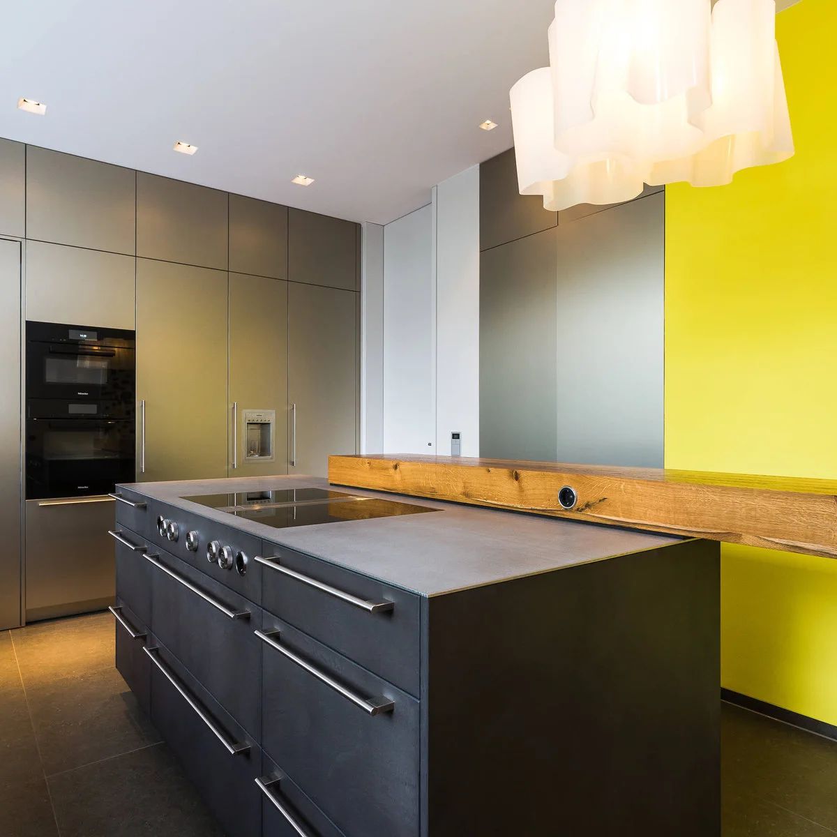 Modern dark kitchen island and tall cabinets beside a bright yellow wall and thick wood-colored ledge