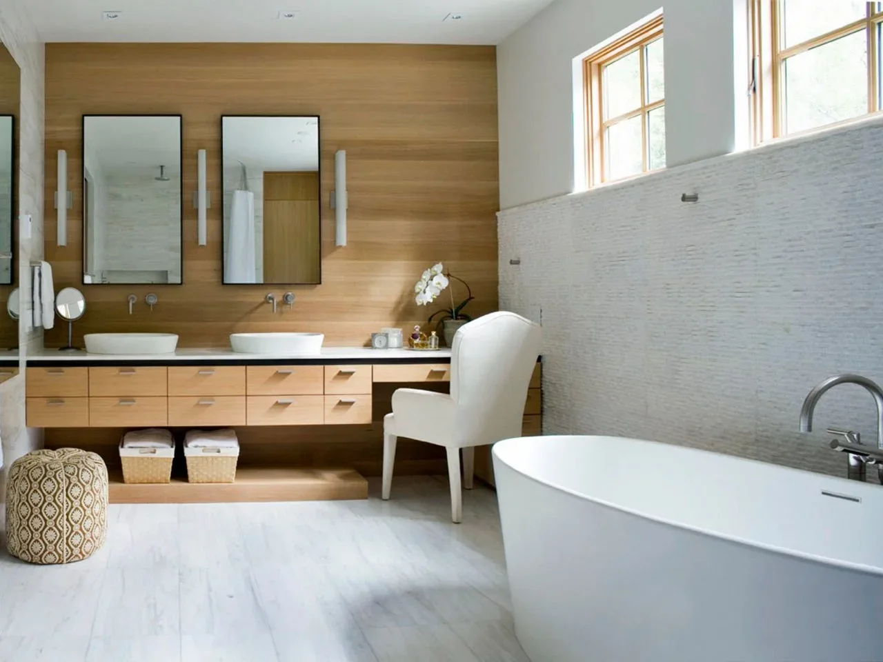 A timber wall and floating vanity sit behind two white basins beside a white tub and textured pale wall.