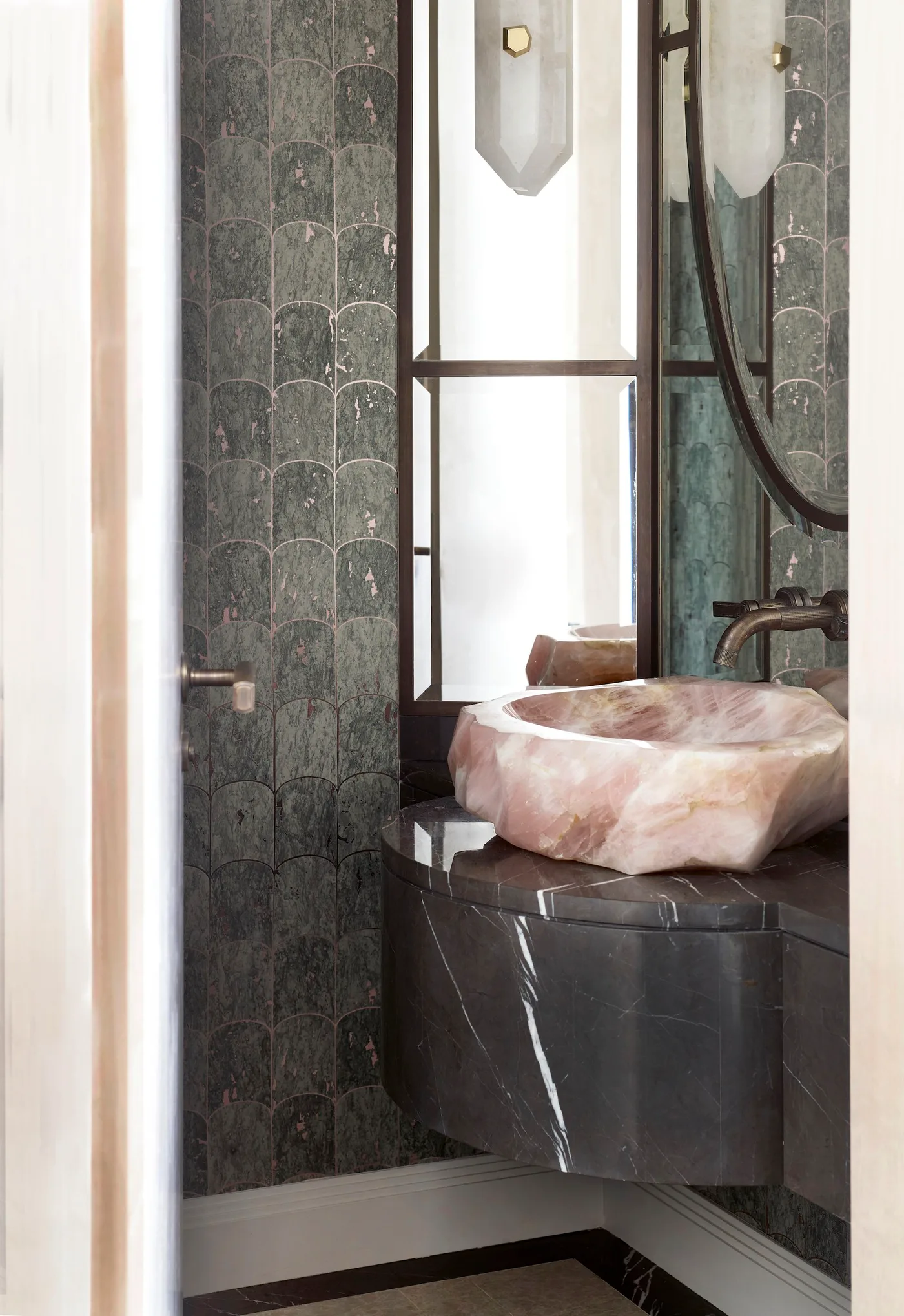 A pink veined bowl basin sits on a dark veined powder-room vanity beside green-gray scalloped wall pattern and dark-framed mirror panels