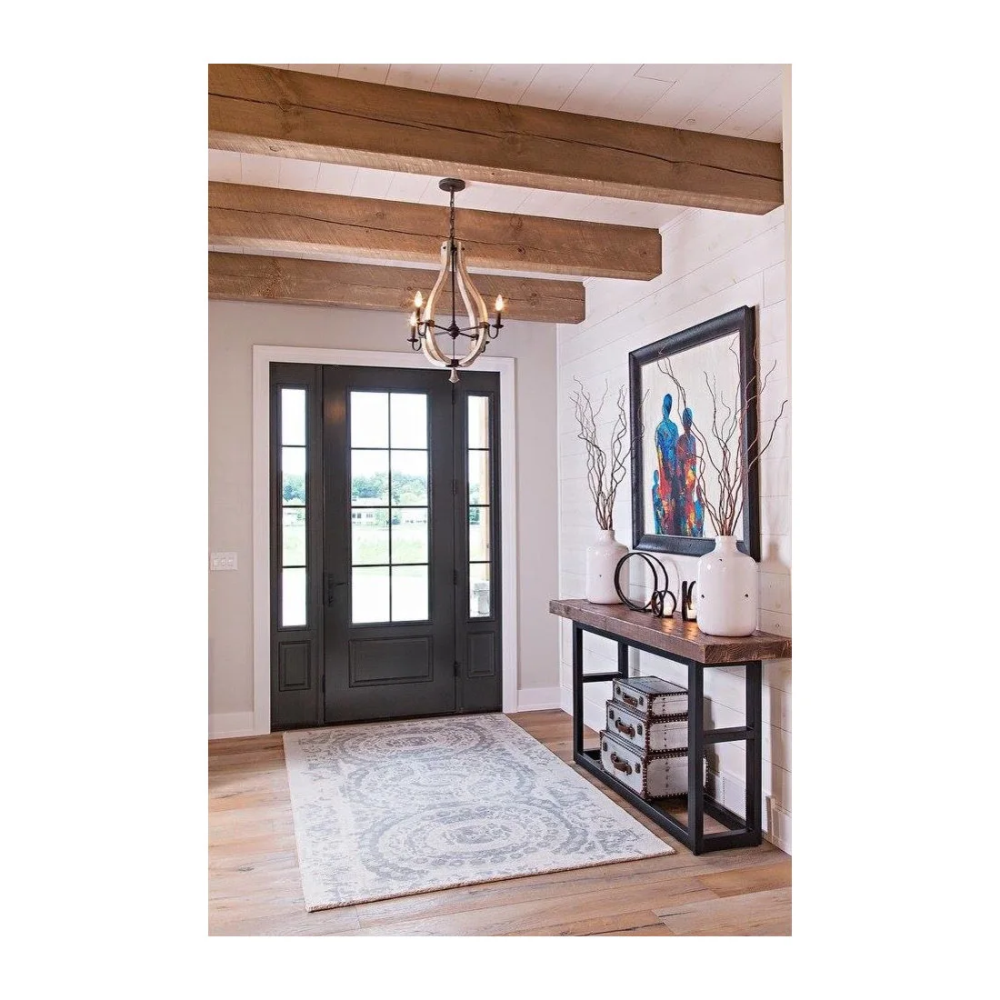 A narrow timber and dark metal console below artwork beside a glazed dark door and white paneling