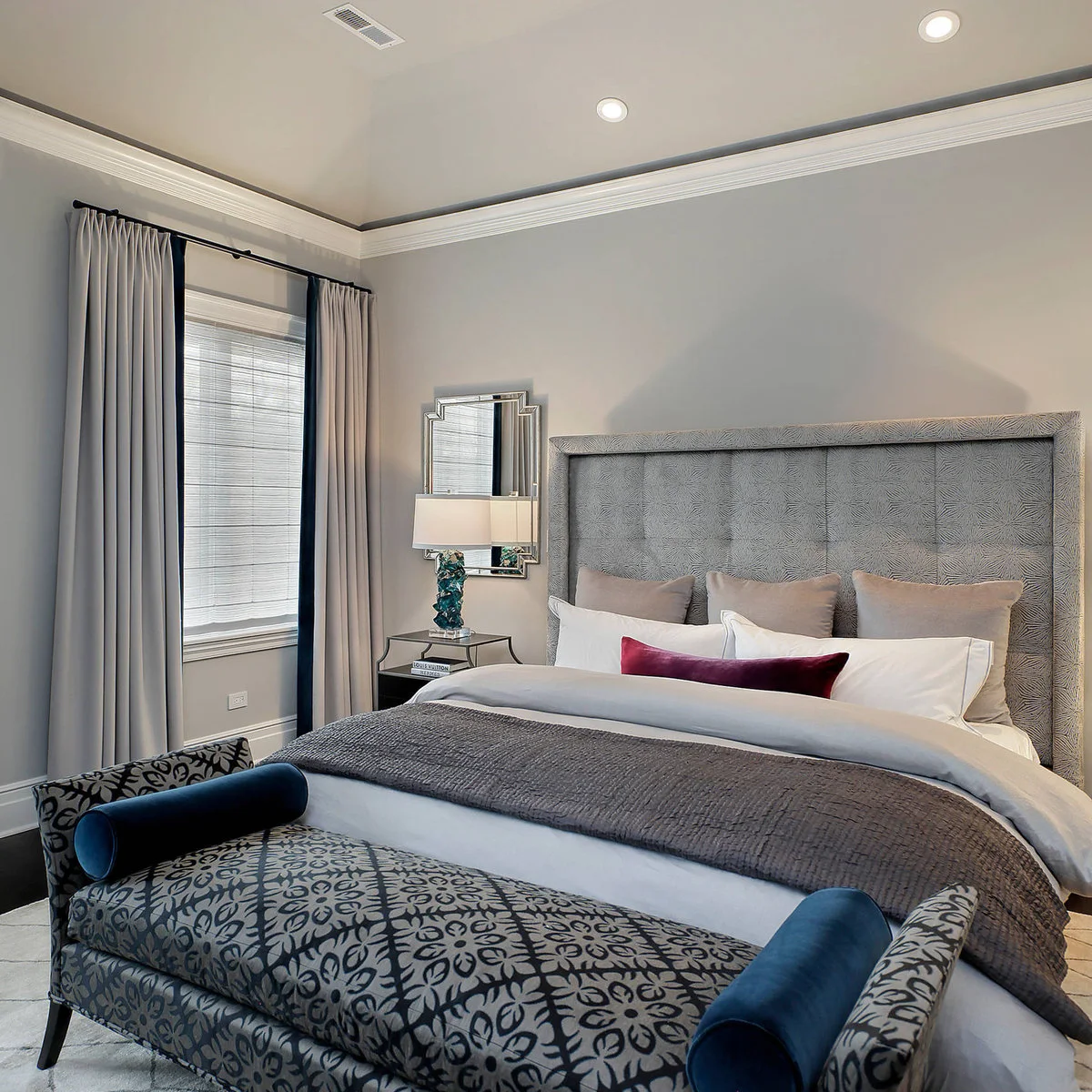 Patterned blue-and-gray bedroom bench with dark blue bolsters at the foot of a pale bed