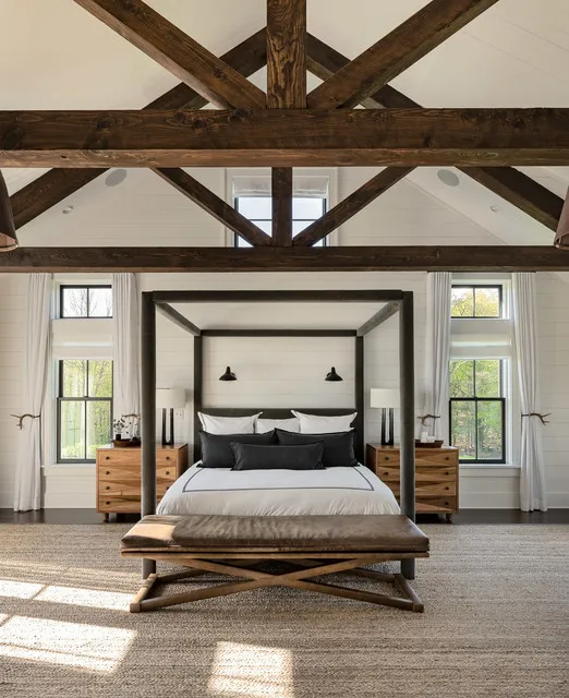 A dark four-poster bed sits beneath substantial timber beams with a modest bench in front.