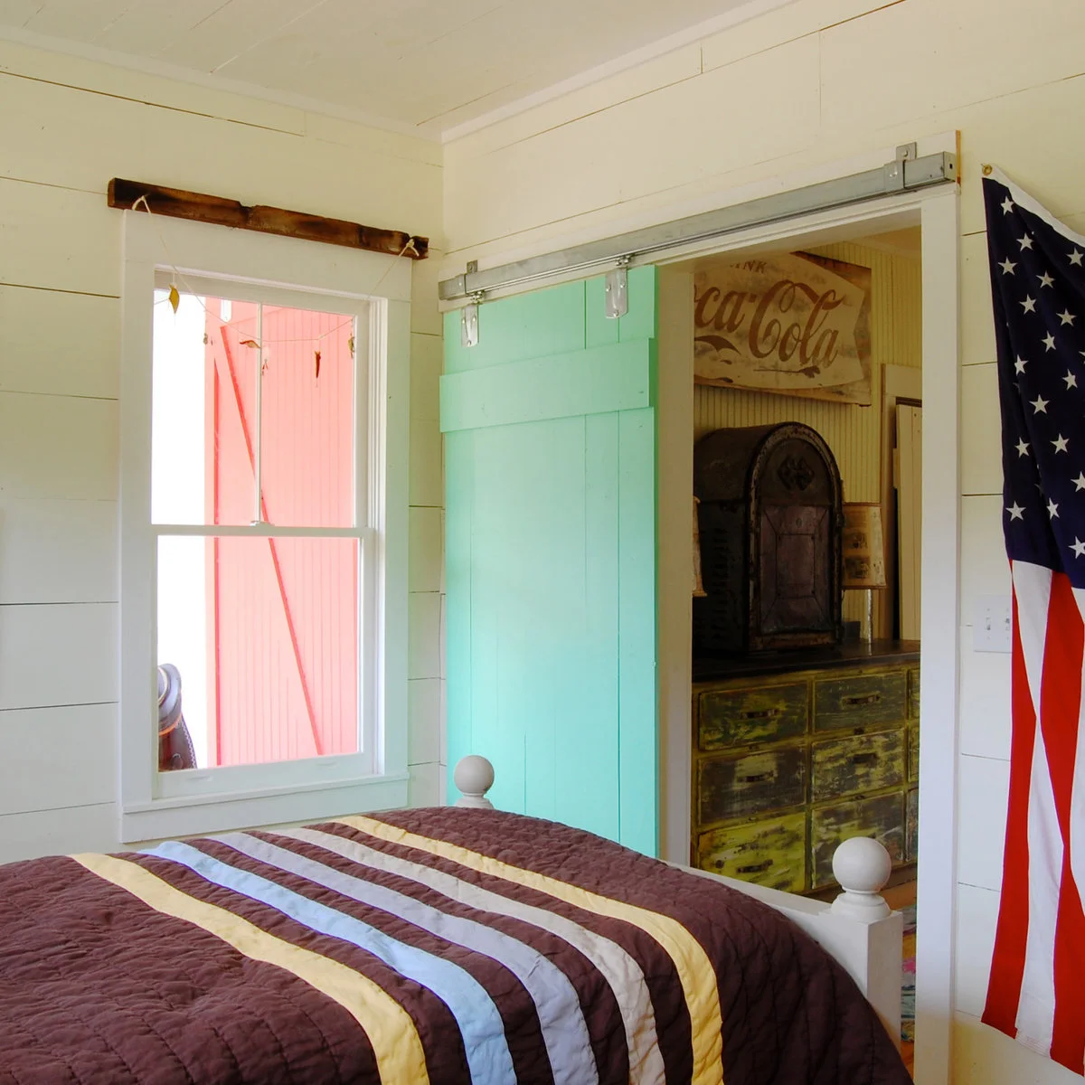 Vintage-style bedroom with a turquoise sliding door, striped cover and worn green storage beyond