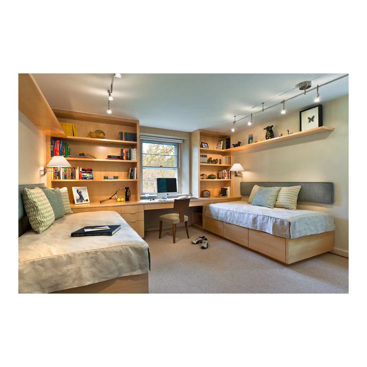 Two low beds facing into a room with a central window desk and wood-colored bookshelves