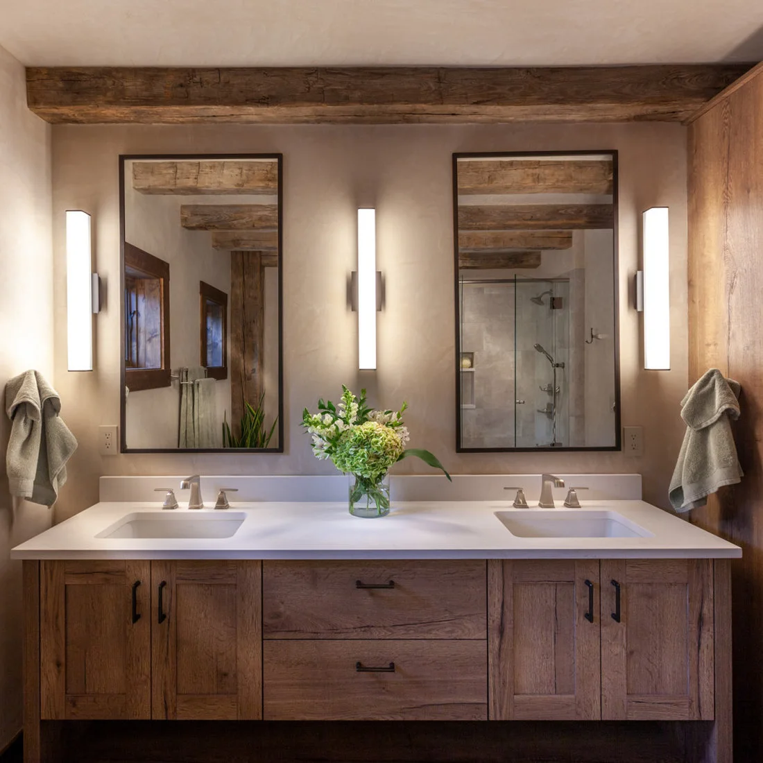 A timber double vanity beneath two narrow mirrors and three vertical lights with beams reflected above