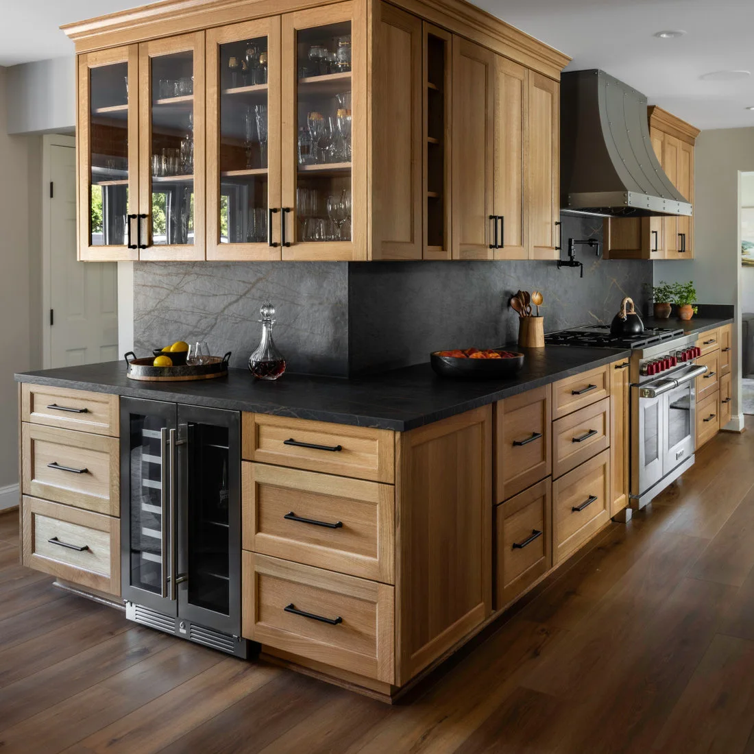 Light wood cabinets with dark counters, slim handles and a curved dark hood