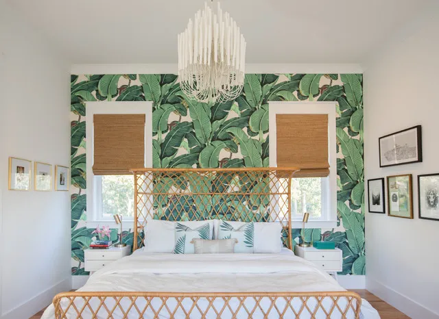 Green banana-leaf wallpaper surrounds two windows behind an open woven bed frame, wood-toned blinds and white bedding