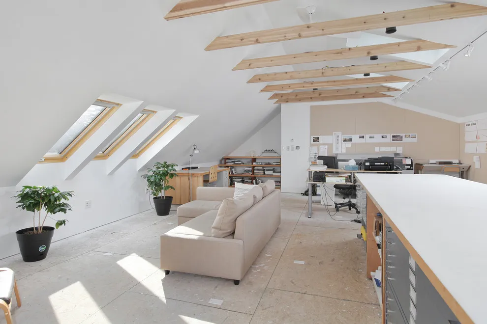 A bright roof-level studio contains long work surfaces beneath skylights and exposed beams