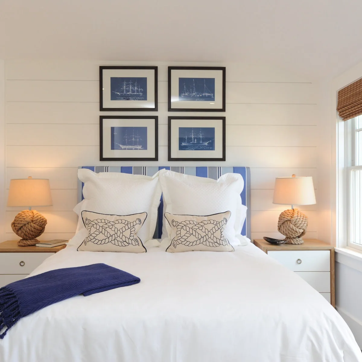 White bedroom with four blue ship prints, a striped headboard and rope-shaped bedside lamps