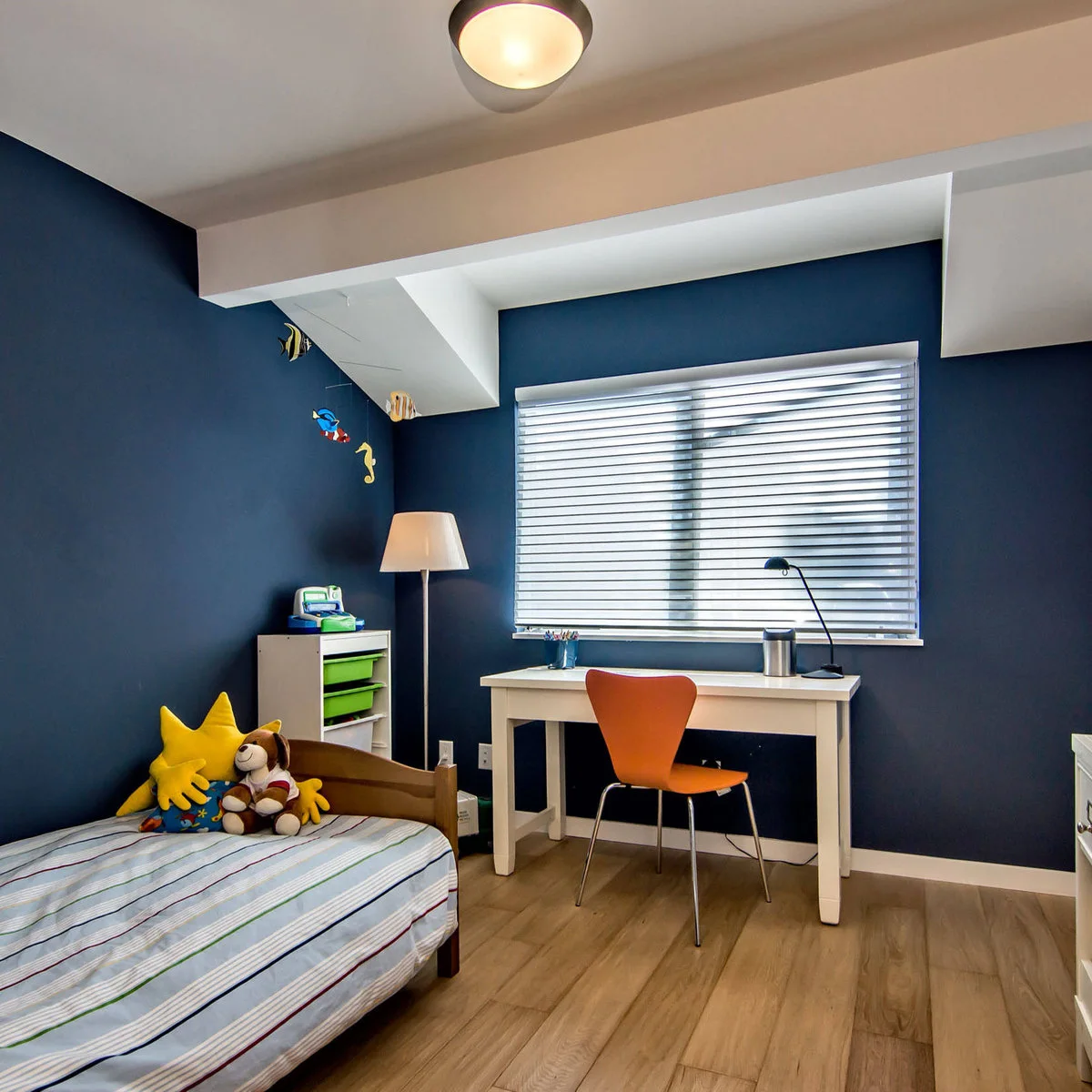 Navy boy’s bedroom with a white window desk, orange chair and green storage trays