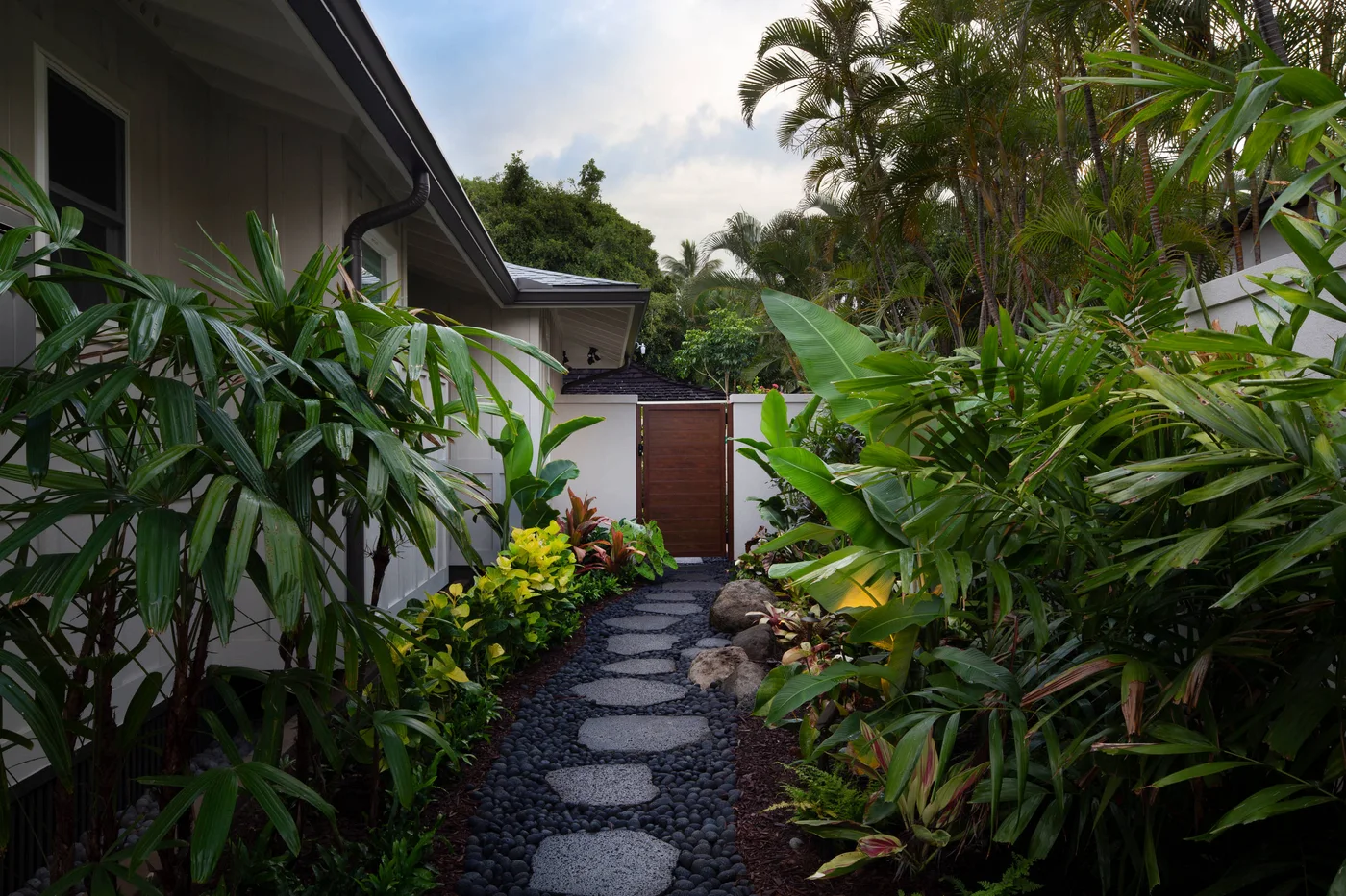 Pale oval stepping surfaces cross dark rounded pebbles in a lush narrow garden passage